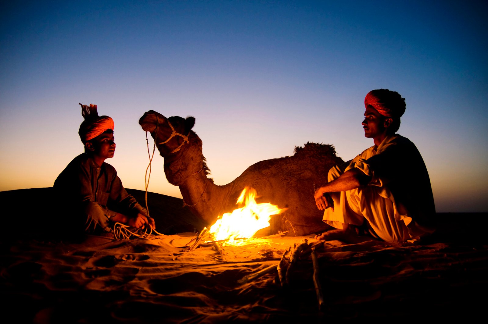 Indian men resting by the bonfire with their camel
